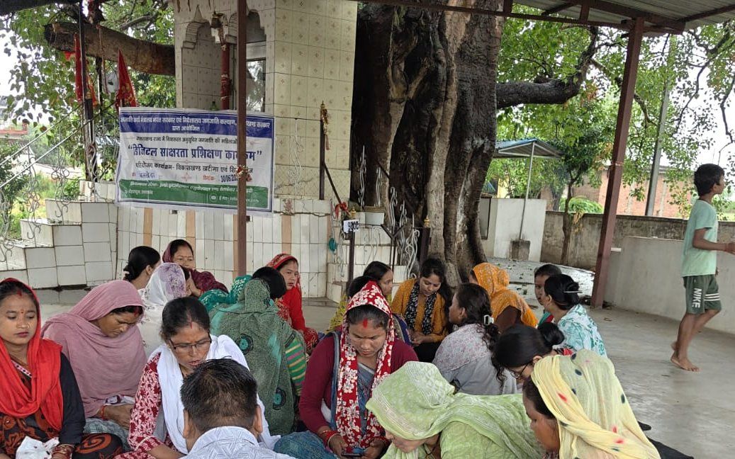 An open-air community awareness session with village residents seated together